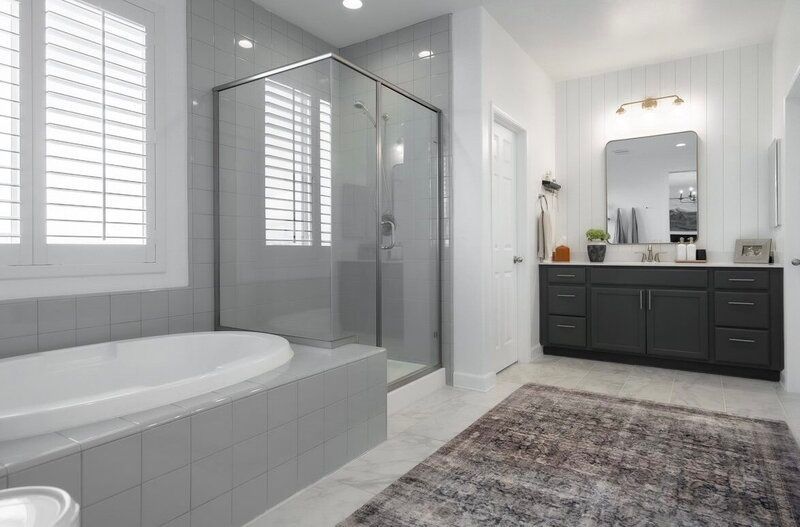 Bathroom with bathtub, glass shower, dark gray vanity, and rug. White walls, gray tile.