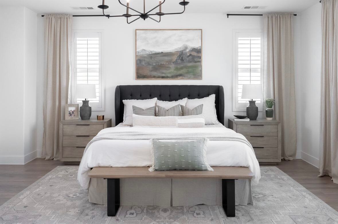 Bedroom with a tufted headboard, neutral bedding, nightstands, and a bench; soft colors and natural light.