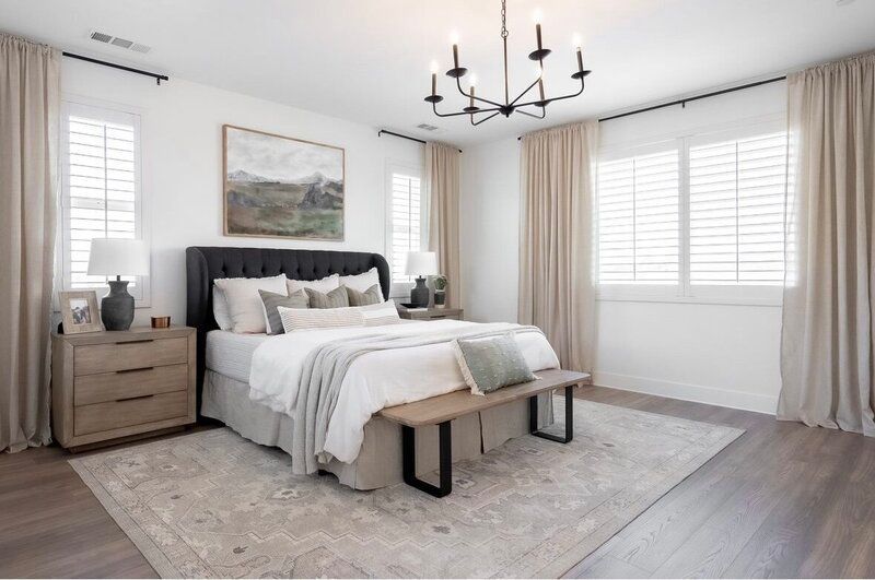 Spacious bedroom with white walls, a tufted headboard, and neutral-toned decor, including a rug and drapes.