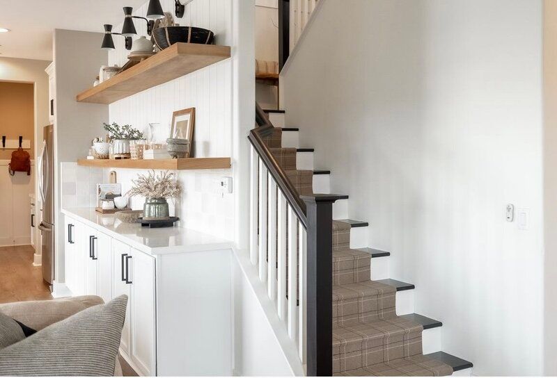 Staircase and white built-in storage with floating shelves. Light wood floors, neutral walls, and black accents.