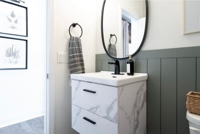 Modern bathroom with marble vanity, black fixtures, oval mirror, and gray and white walls.