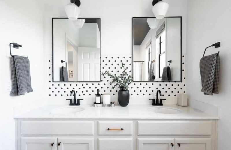 A modern bathroom with a white vanity, black accents, two mirrors, and a black and white polka dot accent wall.