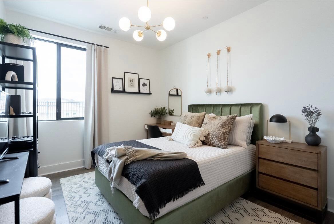 Bedroom with a green velvet bed, white walls, and a black bookshelf.