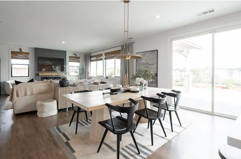 Open-concept dining and living area. White table and black chairs, large windows, and neutral colors.
