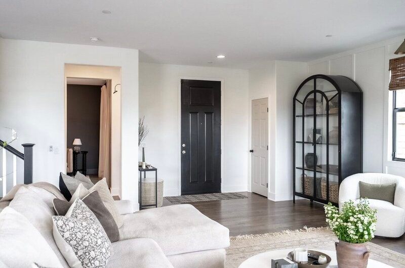 Living room with white walls, dark door, and black display cabinet. Beige sofa and round coffee table.