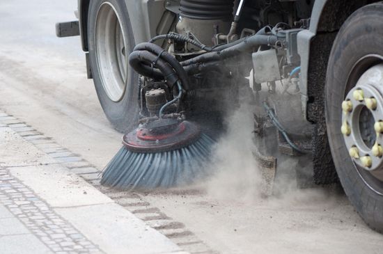 a truck is cleaning the sidewalk with a brush