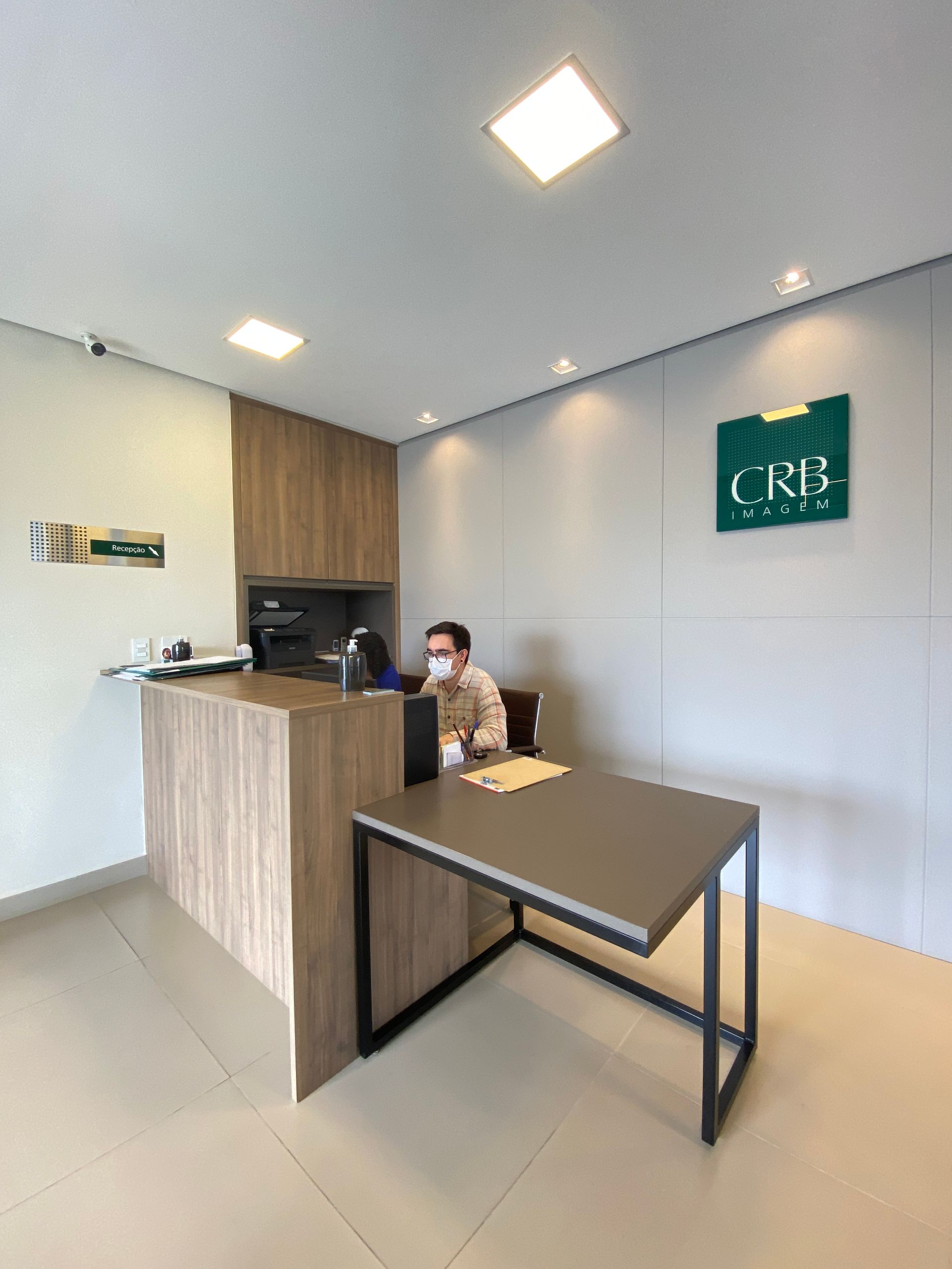 Recepcionista em uma mesa com extensão; tons de madeira e cinza em um escritório moderno.