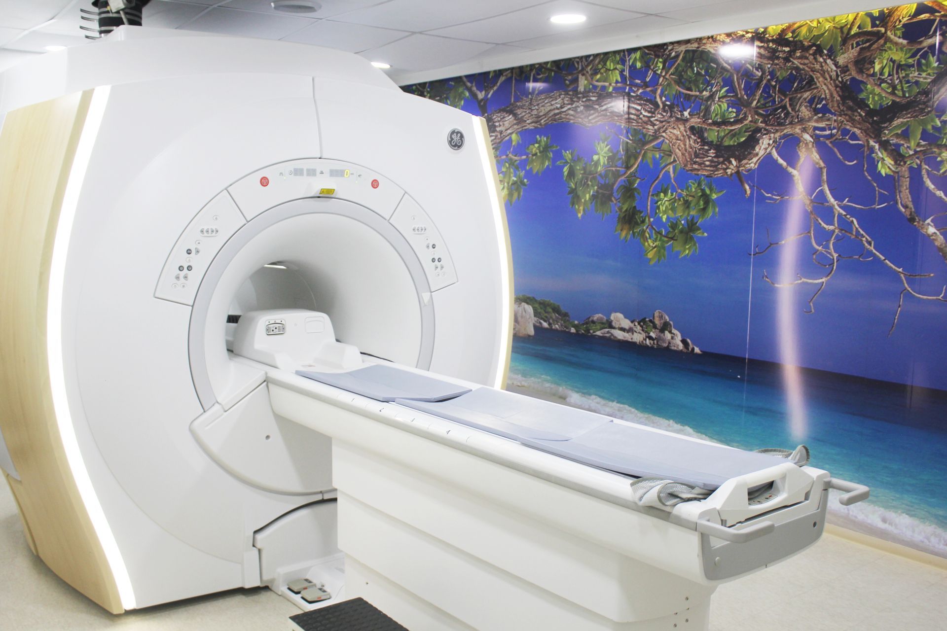 Aparelho de ressonância magnética em uma sala bem iluminada com um mural de praia na parede.