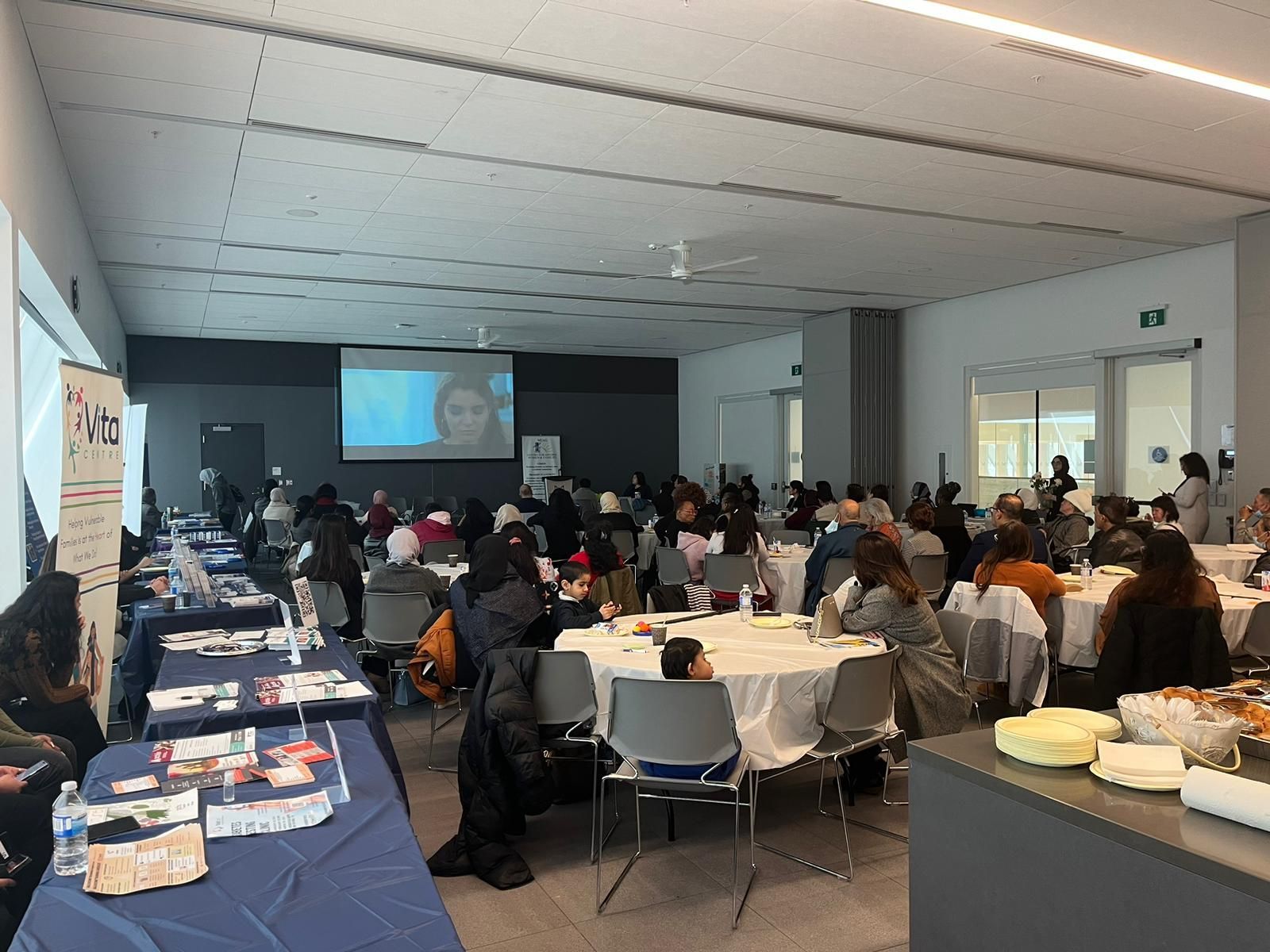 A large room filled with people sitting at tables and chairs.