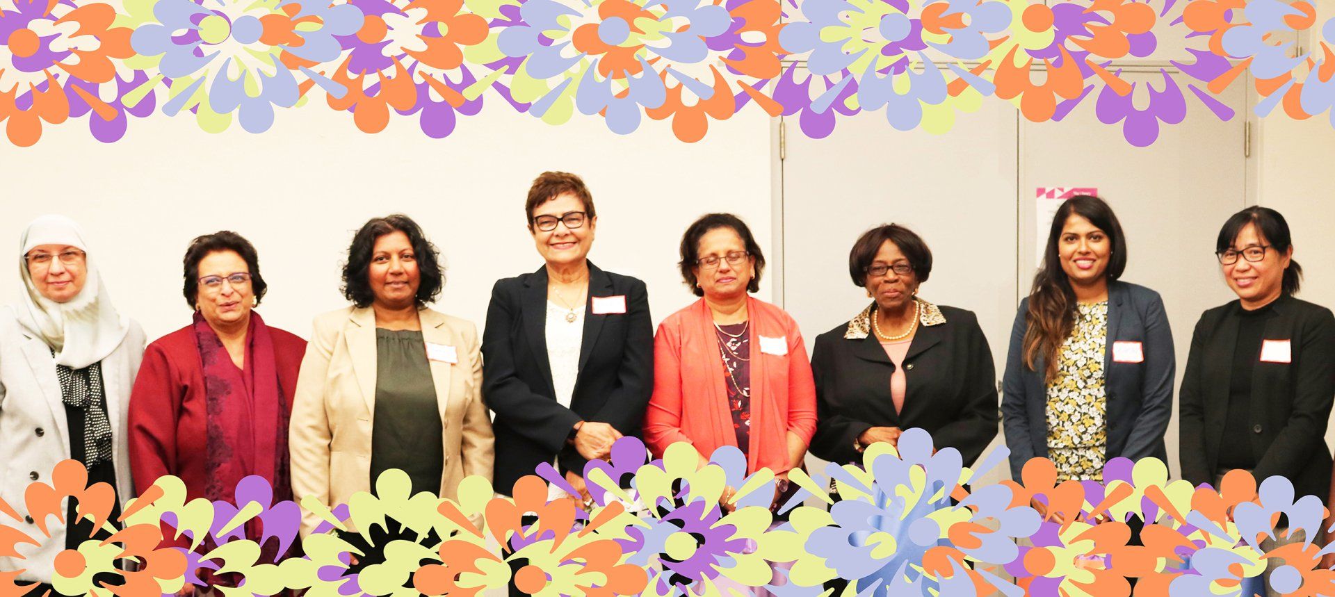 A group of women are standing next to each other in front of flowers.