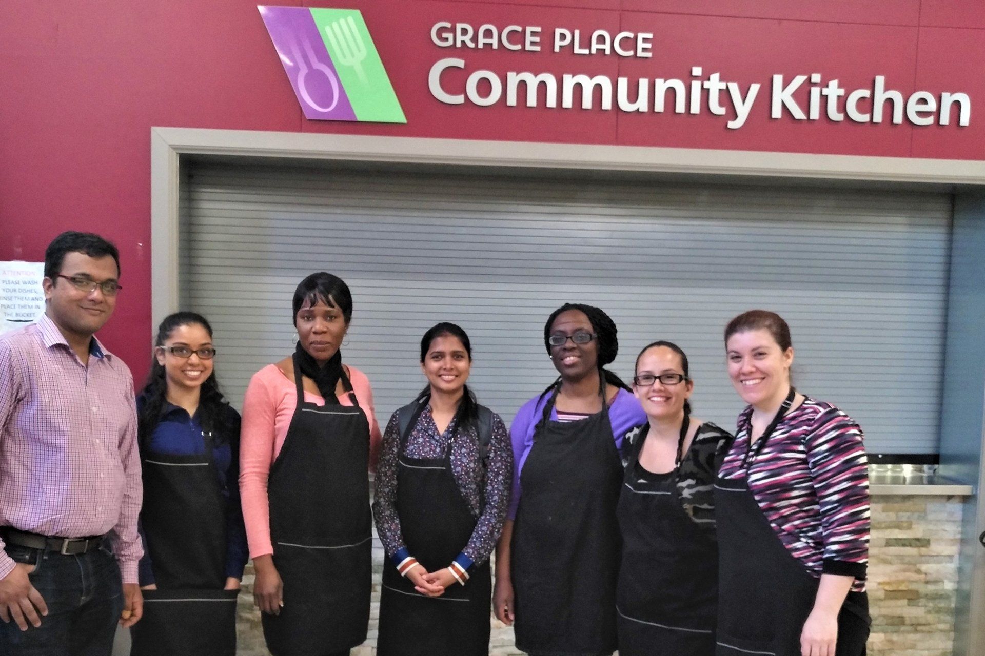 A group of people are posing for a picture in front of the grace place community kitchen.
