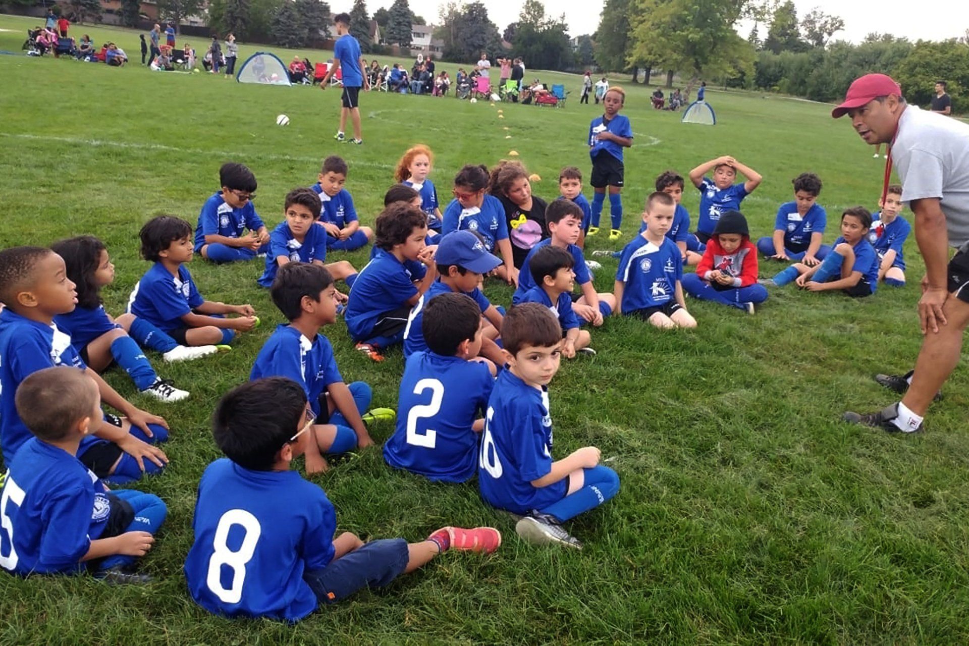 A group of young boys wearing blue jerseys with the numbers 2 and 8 sitting on the grass