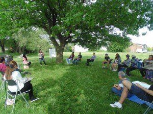 A group of people are sitting in a circle in the grass under a tree.