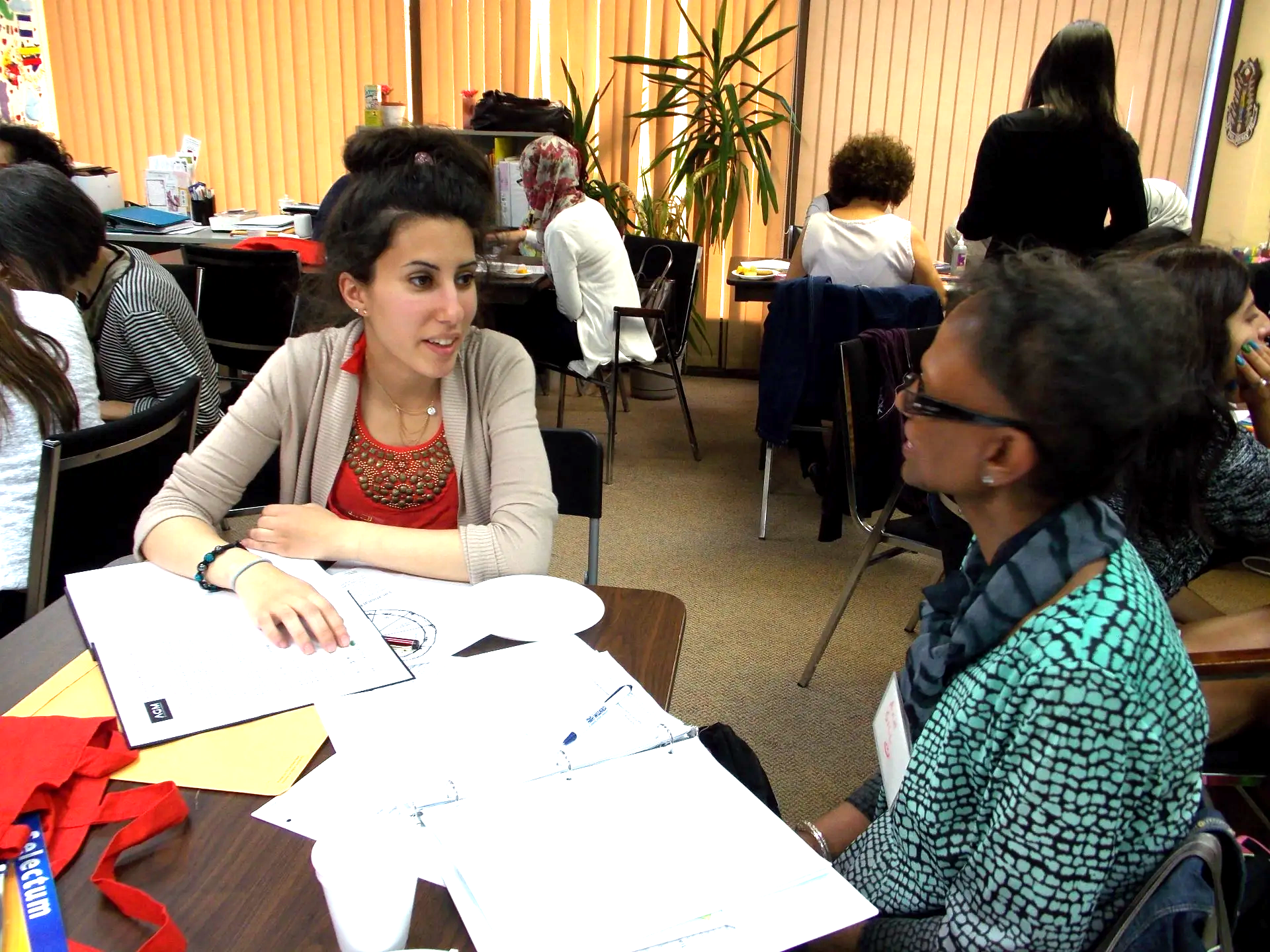 Two women are sitting at a table talking to each other
