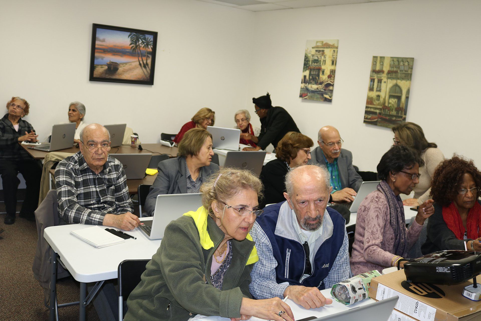 A group of people are sitting at tables with laptops in a room.