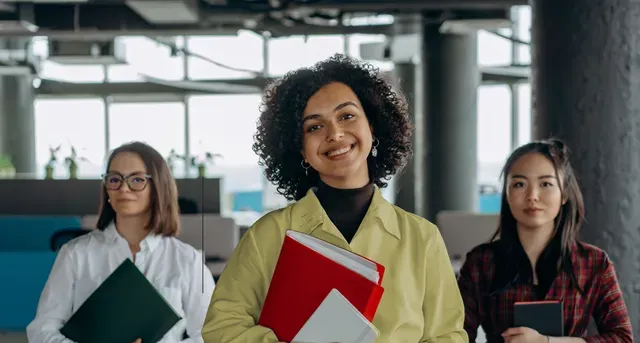 Three women are standing next to each other in a room holding books.