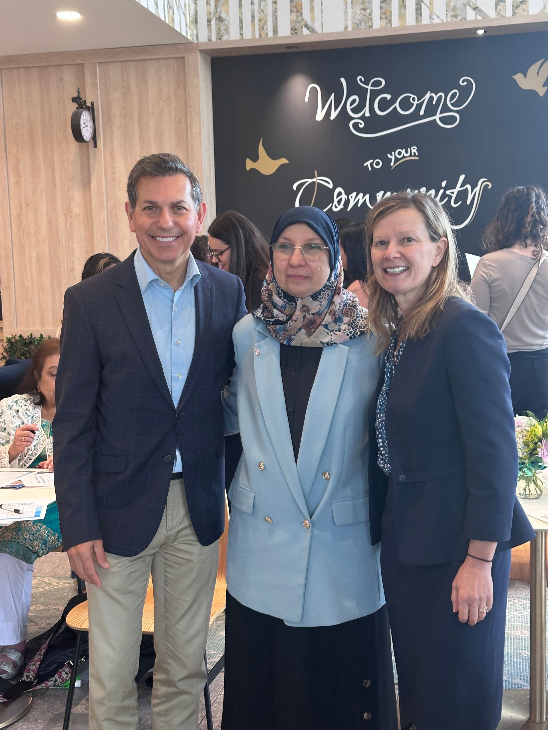 Three people smiling, posing together in a brightly lit room with a 