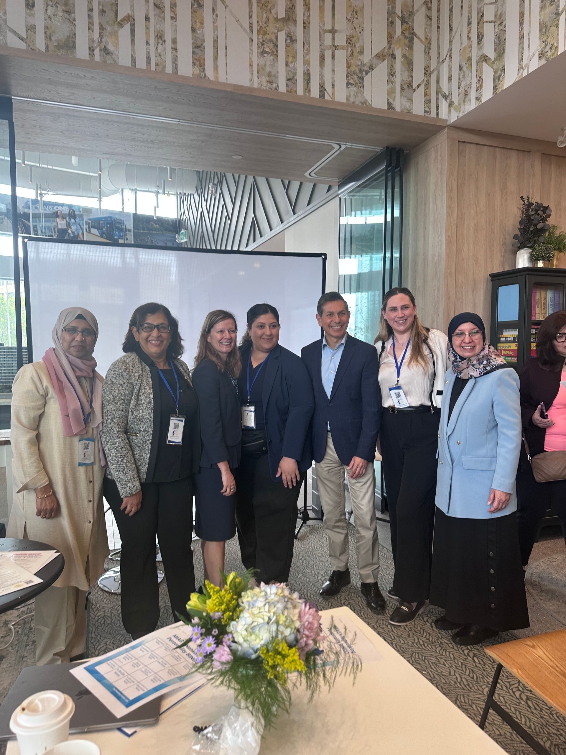 Group of diverse people posing indoors for a photo in front of a screen and flowers.