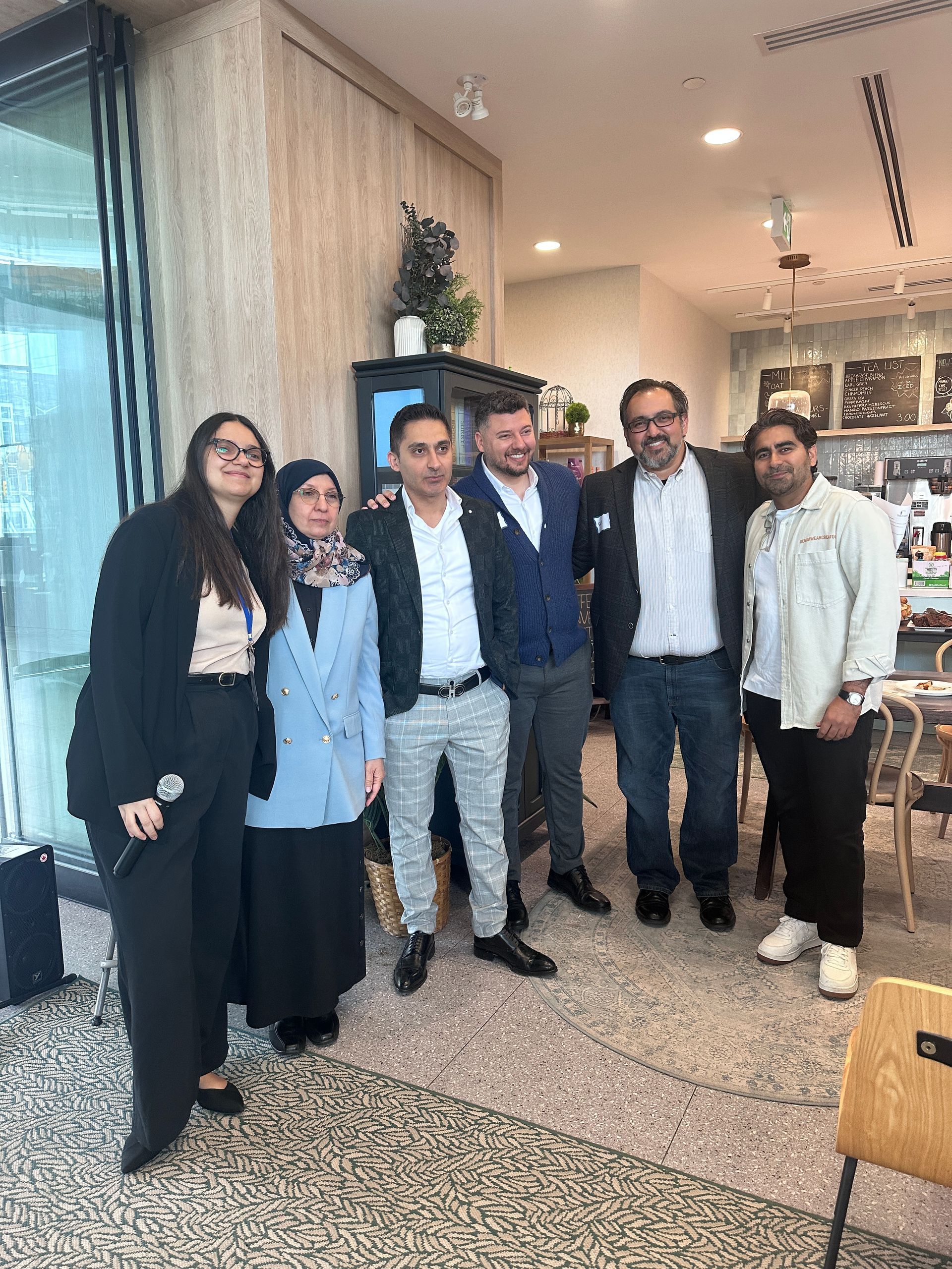 Group of six people posing indoors: three men, three women. Neutral setting, smiling.