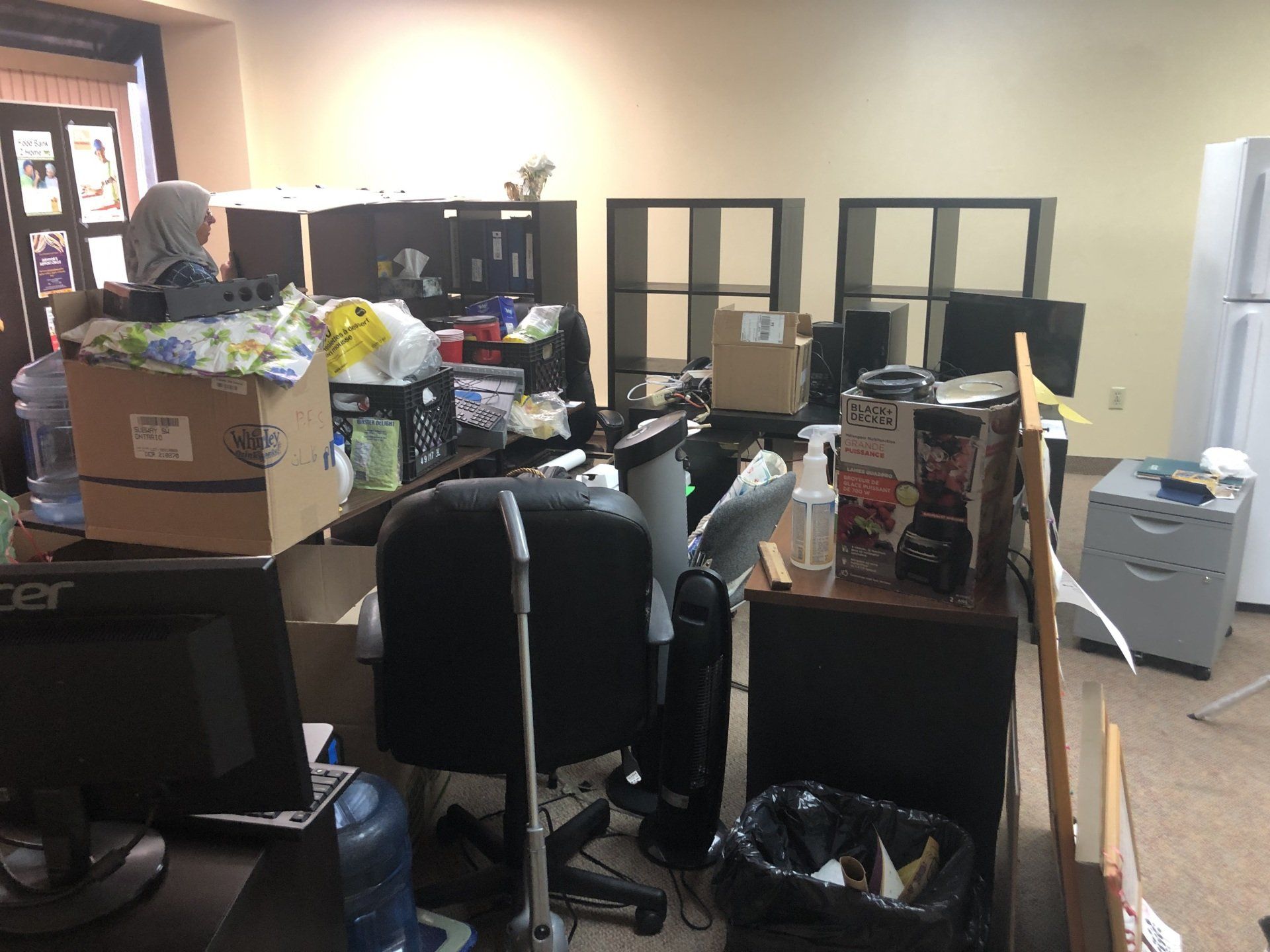 A messy office with boxes on the desks and chairs.