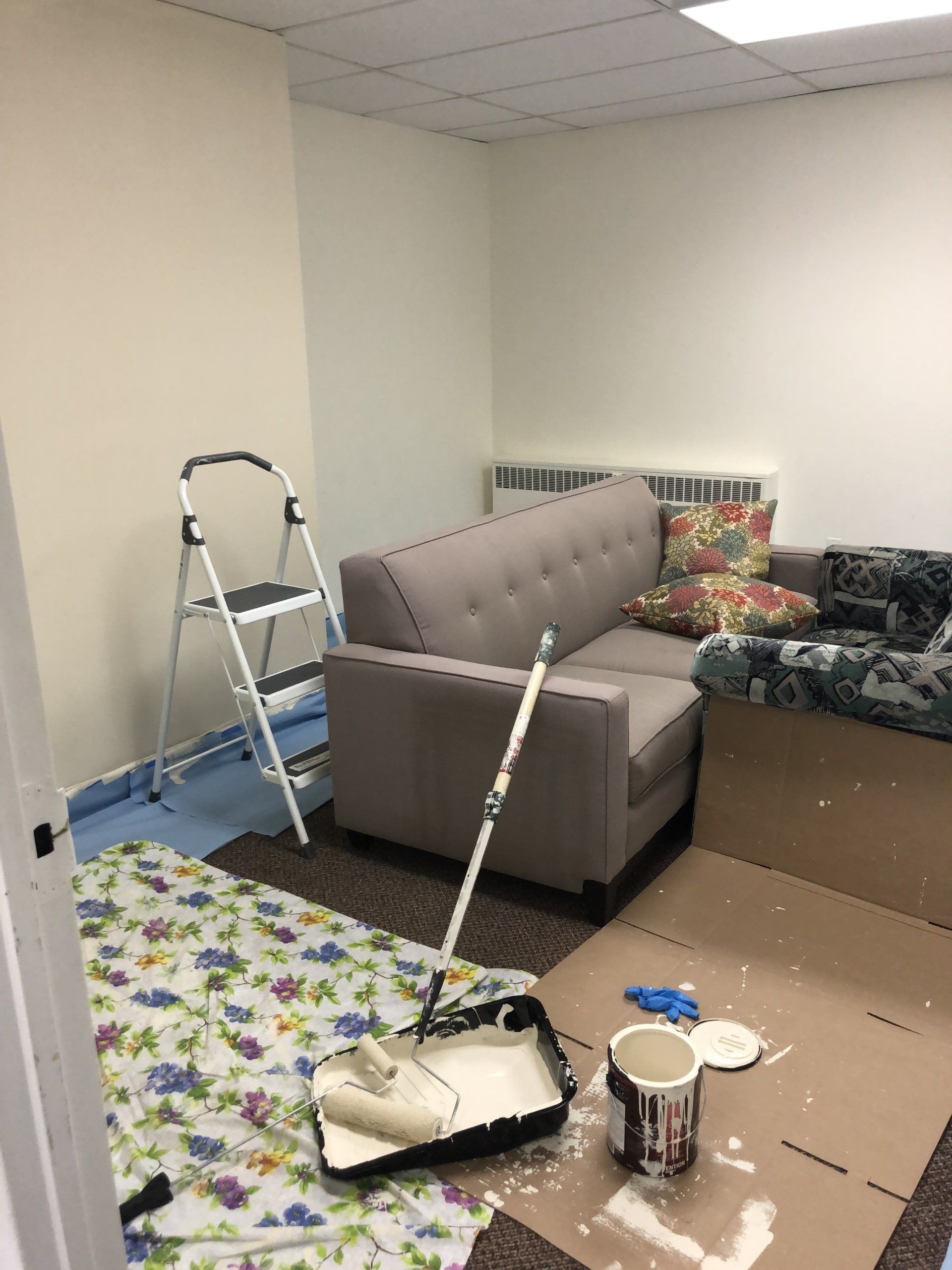 a living room with a couch , chair , and ladder being painted .