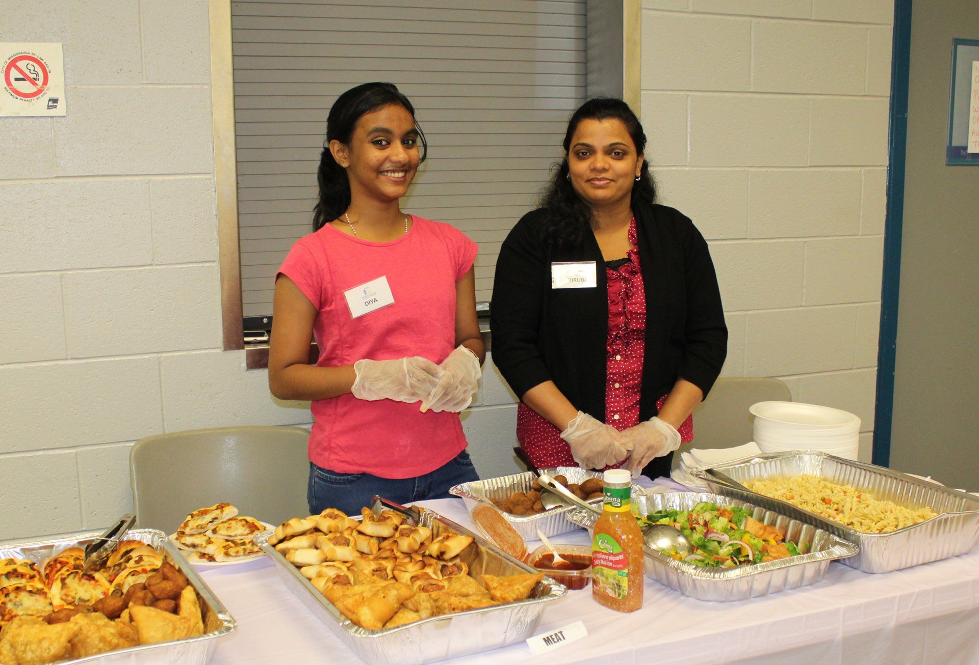 Two women are standing in front of a table full of food.