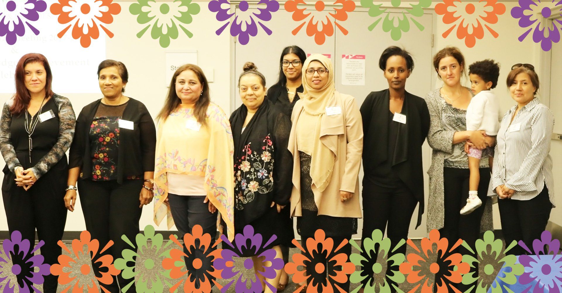 A group of women standing next to each other in front of a wall with flowers on it.
