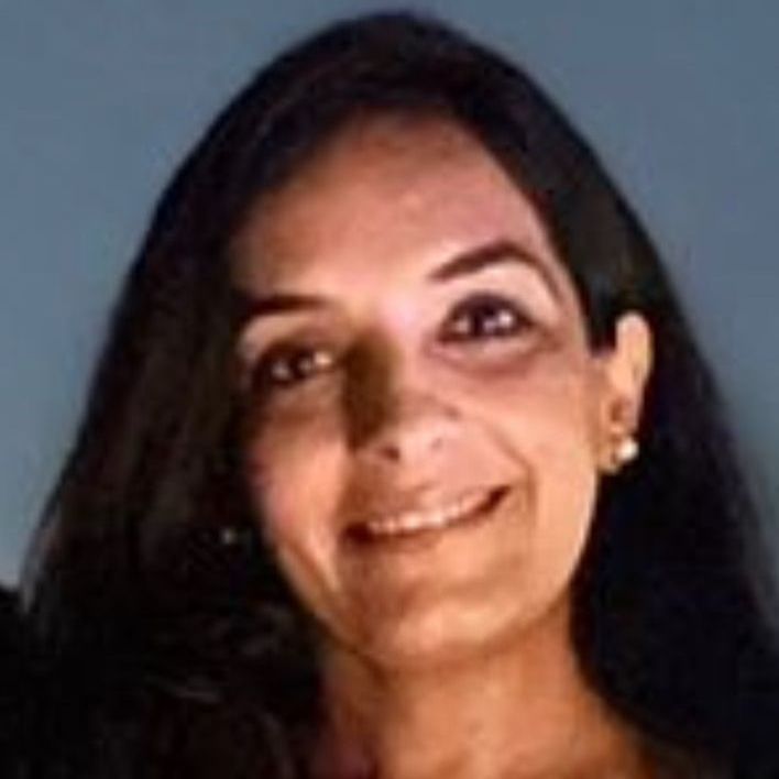 A woman in a suit and necklace is smiling for the camera.