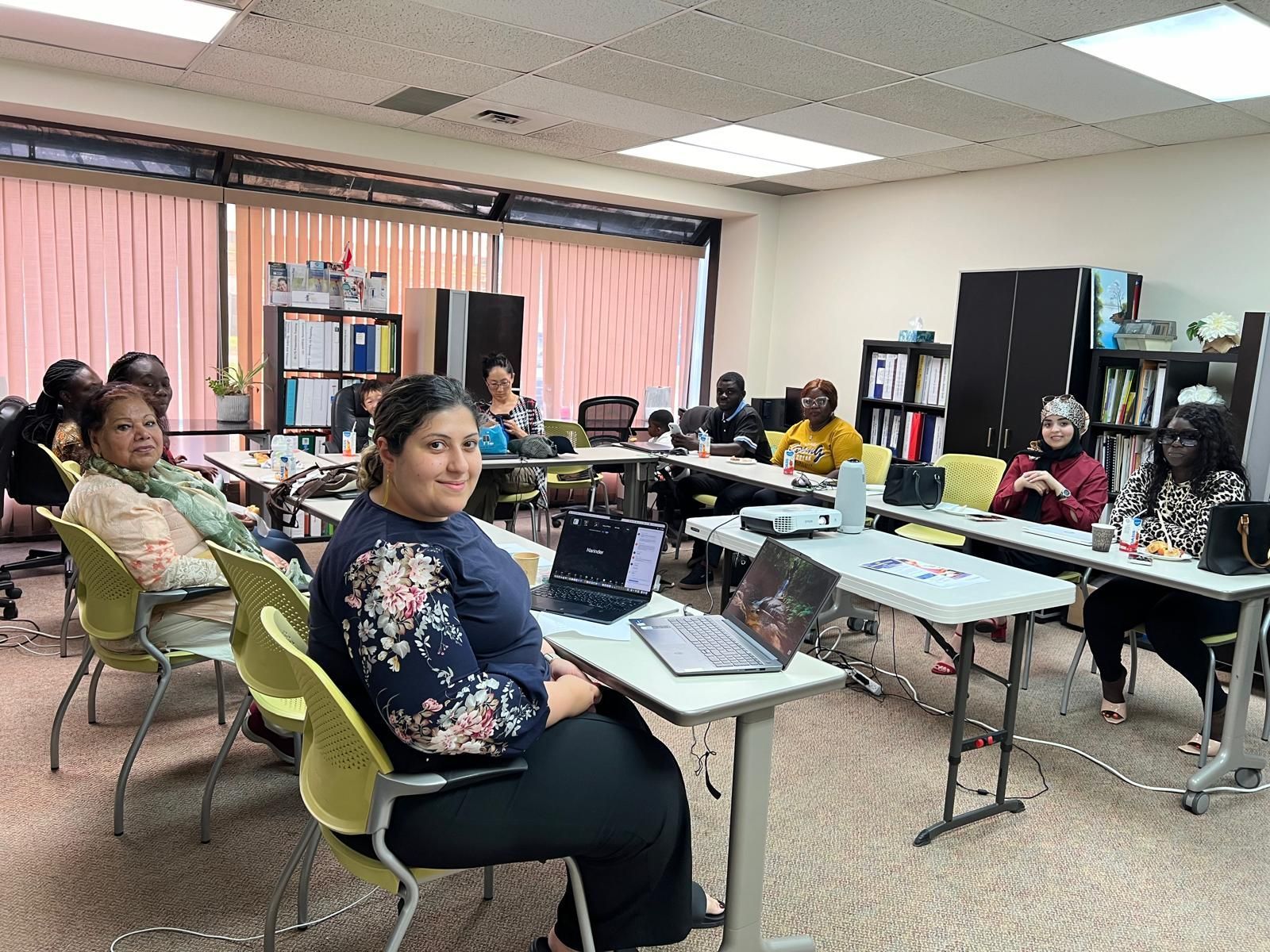 A group of people are sitting at tables in a room with laptops.