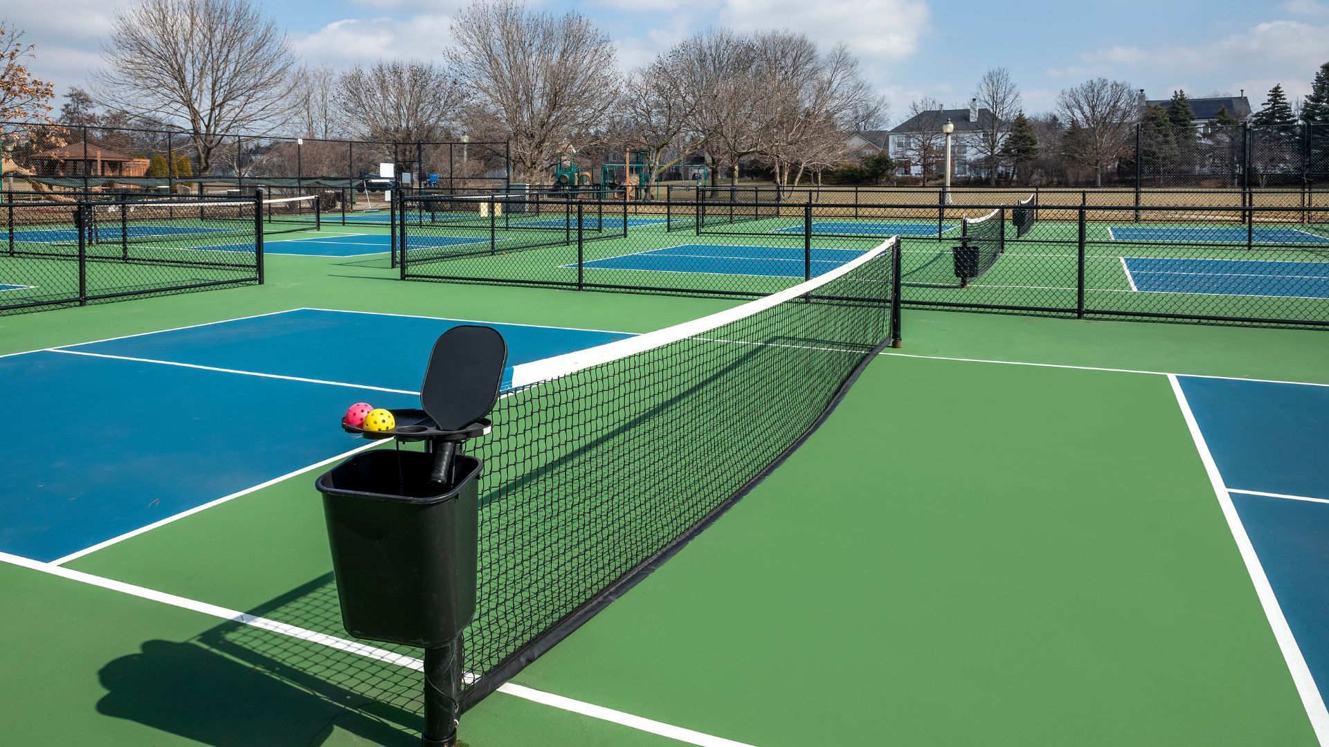 Outdoor pickleball courts with blue and green surfaces and nets, seen on a sunny day.