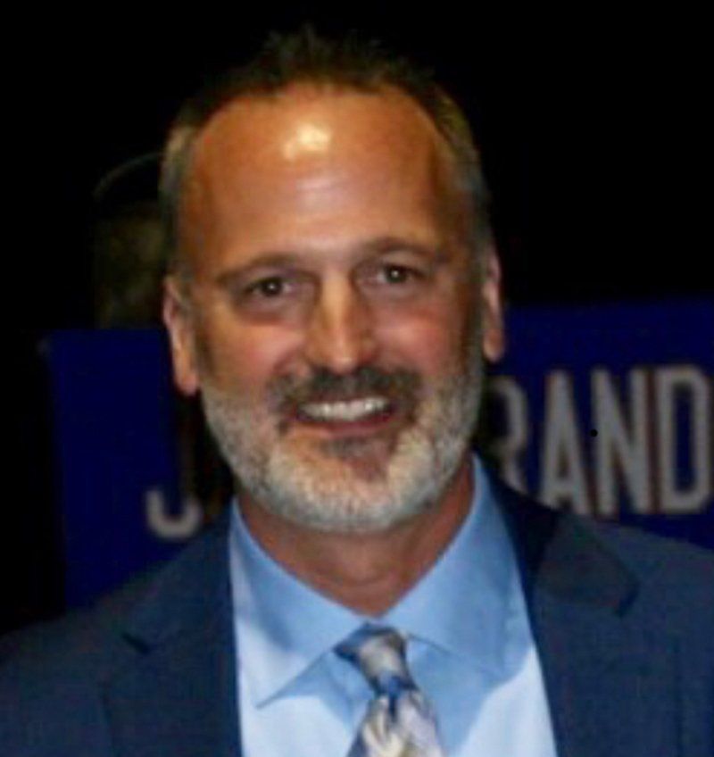 A man in a suit and tie is smiling in front of a sign that says rand