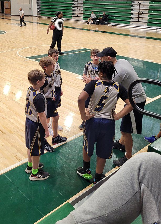 A group of young boys are standing on a basketball court talking to each other.
