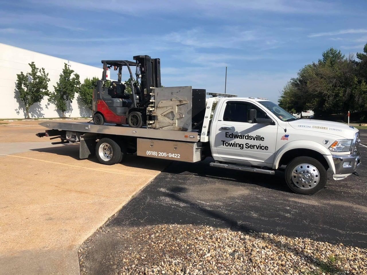 a white edwardsville towing service truck is carrying a forklift