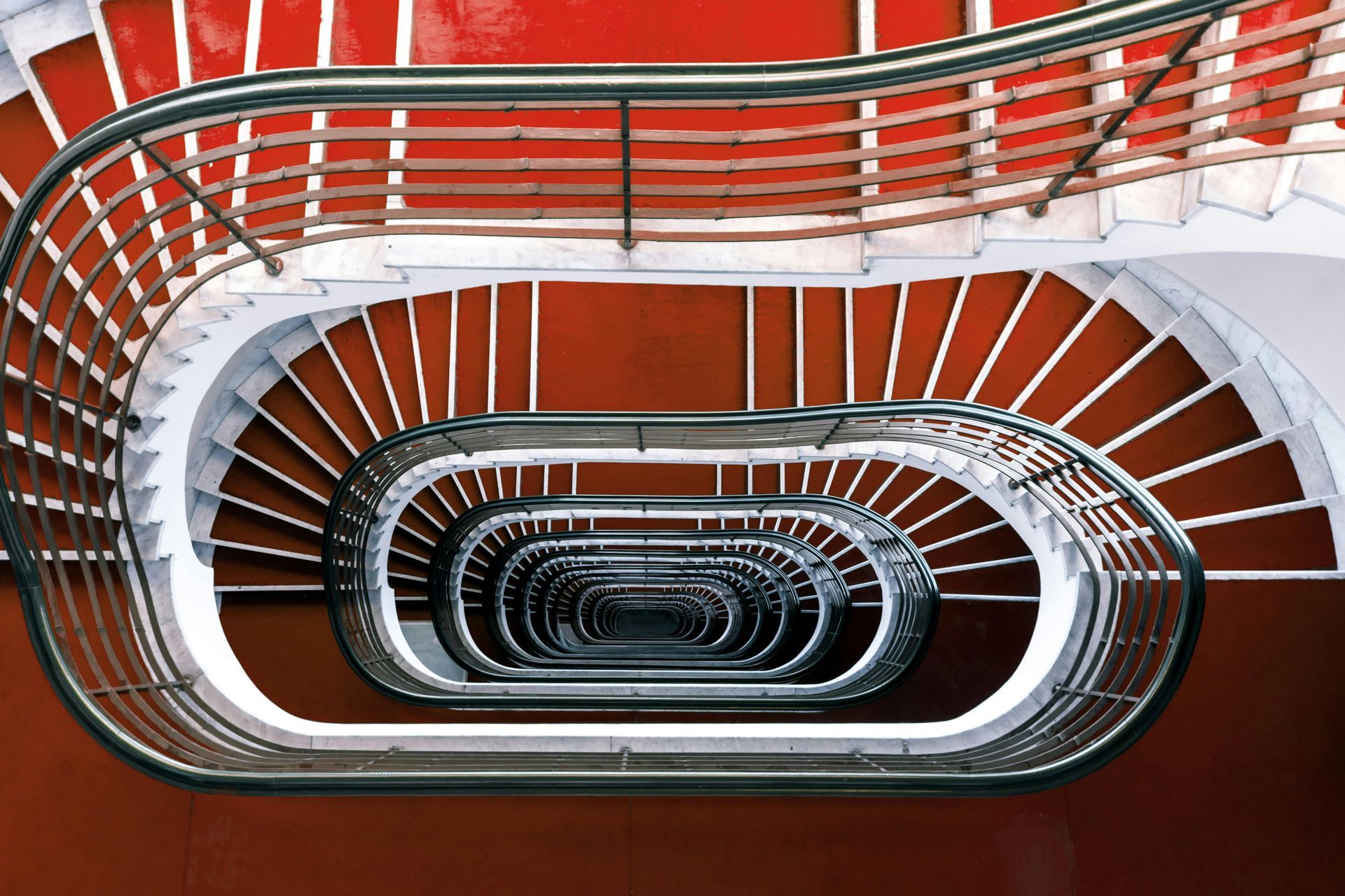 A spiral staircase with a red carpet and a stainless steel railing