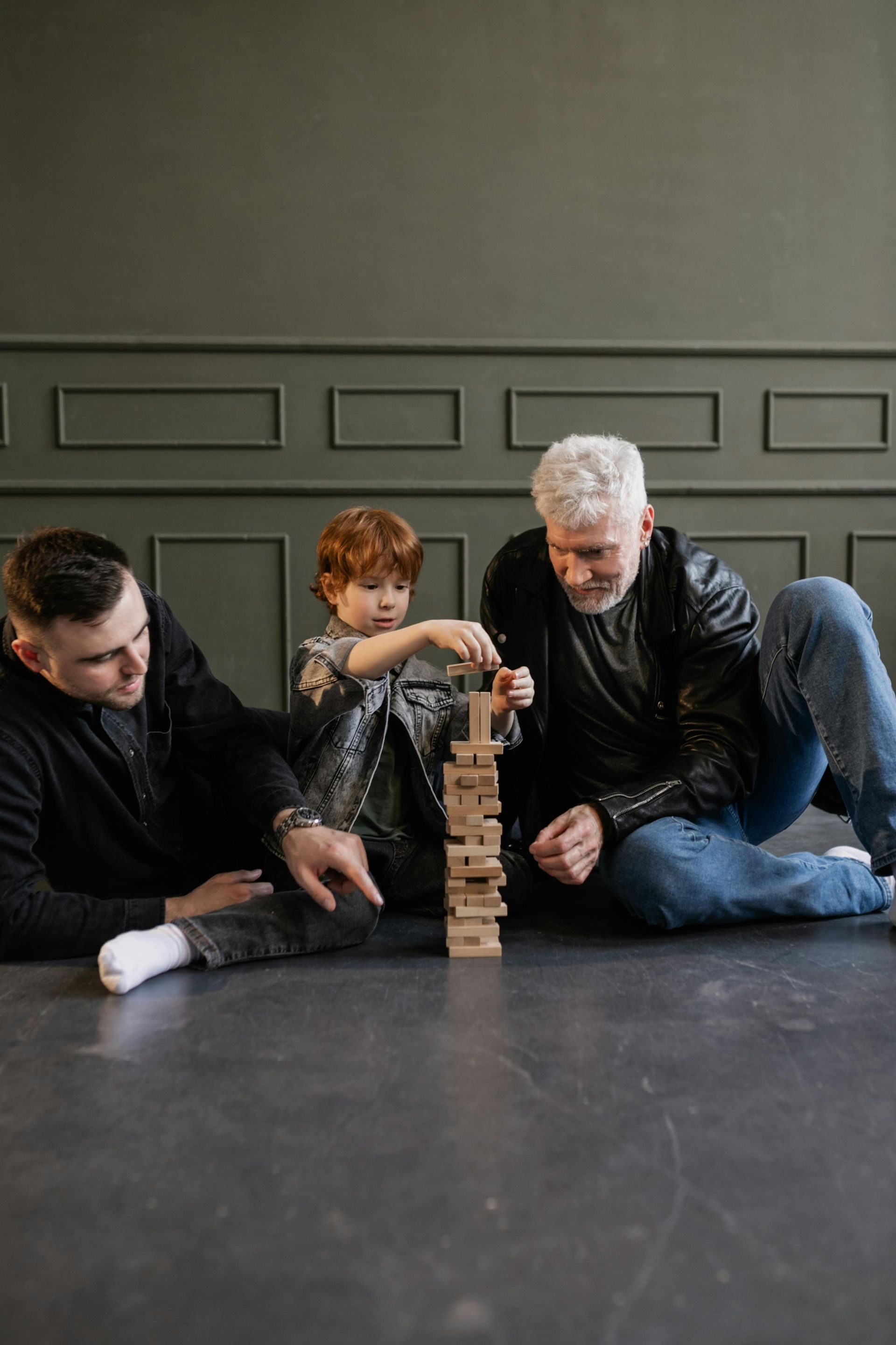 Two men and a child are sitting on the floor playing with wooden blocks.