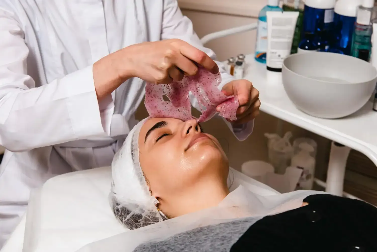 A person receiving a facial treatment. A esthetician applies a mask to the client's face.