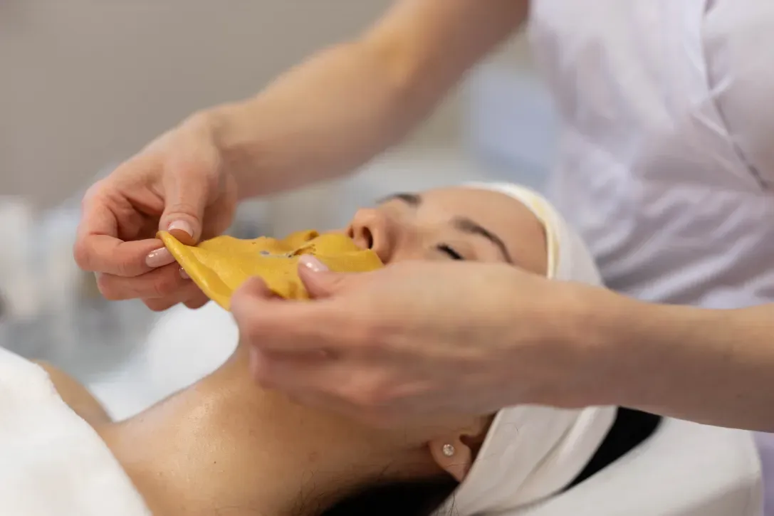 A person receiving a facial treatment. A esthetician applies a mask to the client's face.