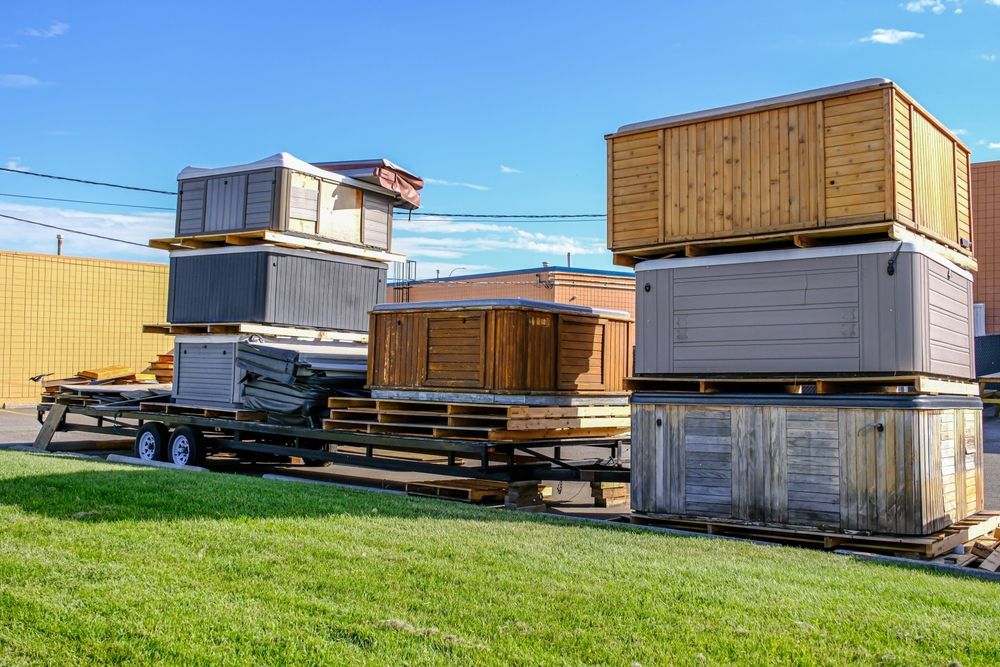 A trailer loaded with several hot tubs in various colors, stacked on pallets, outside on a sunny day.