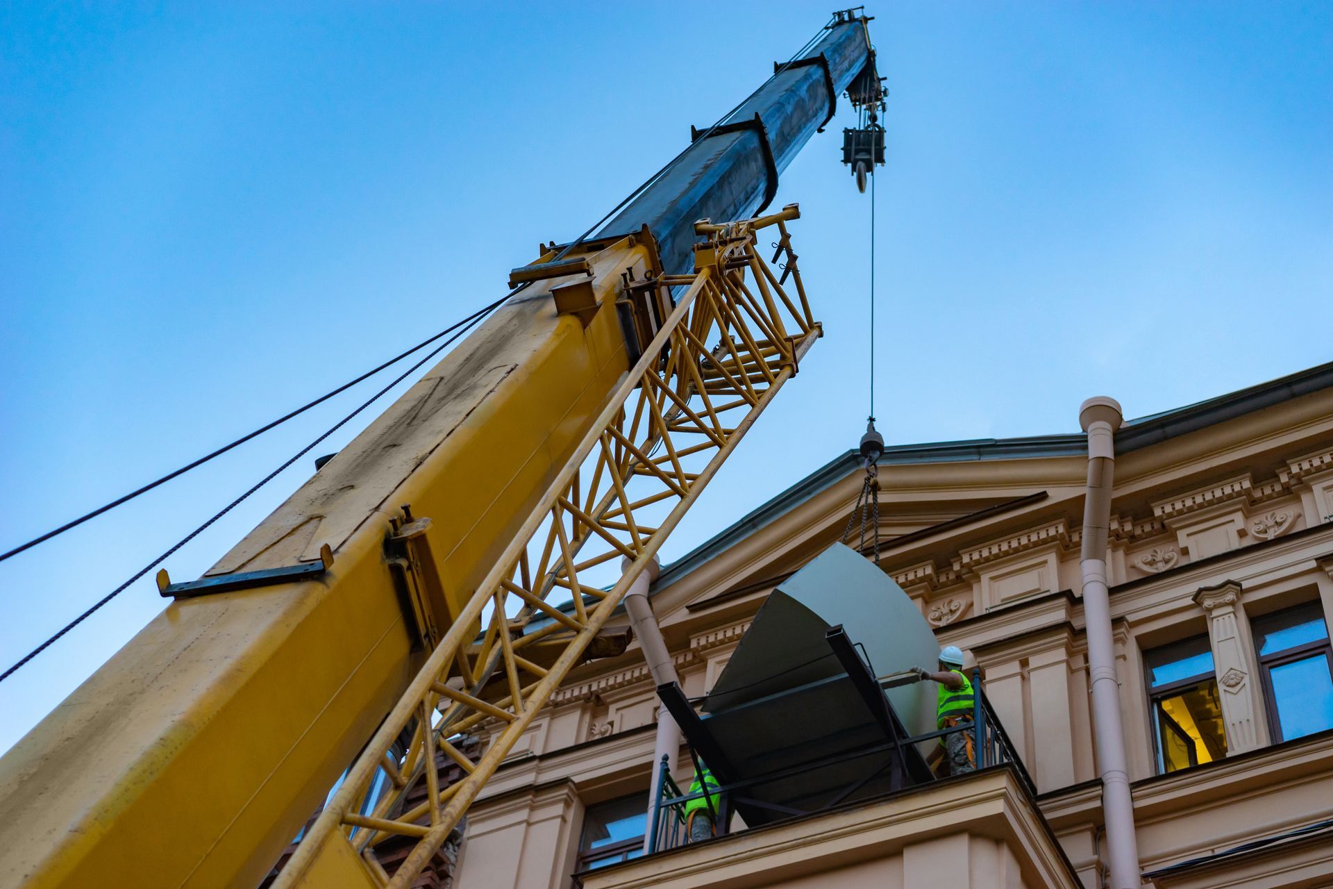 Crane lifting equipment onto a building roof; construction workers are present, blue sky.