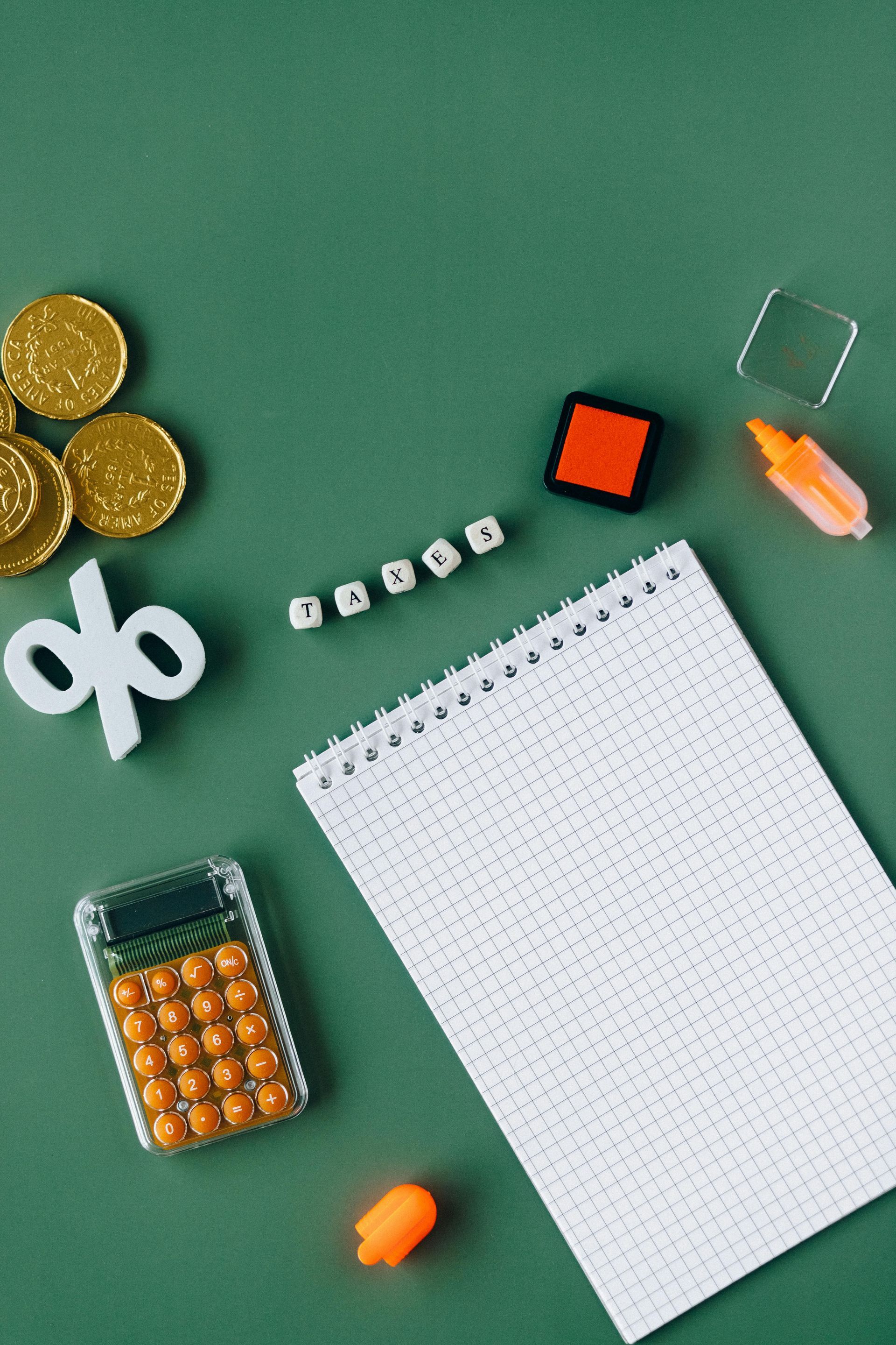 A notebook , calculator , dice , and coins are on a green table.