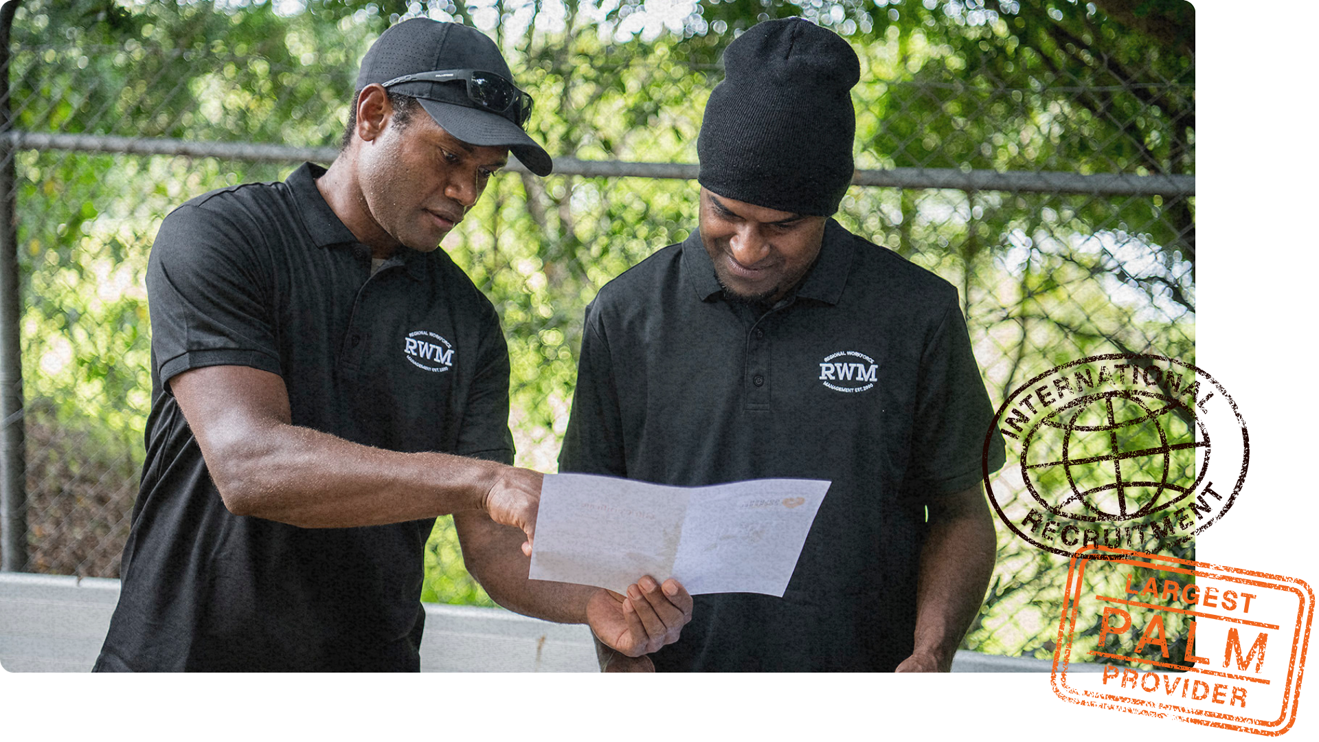 Two workers in black RWM shirts reviewing information on certificates, one pointing while the other observes.