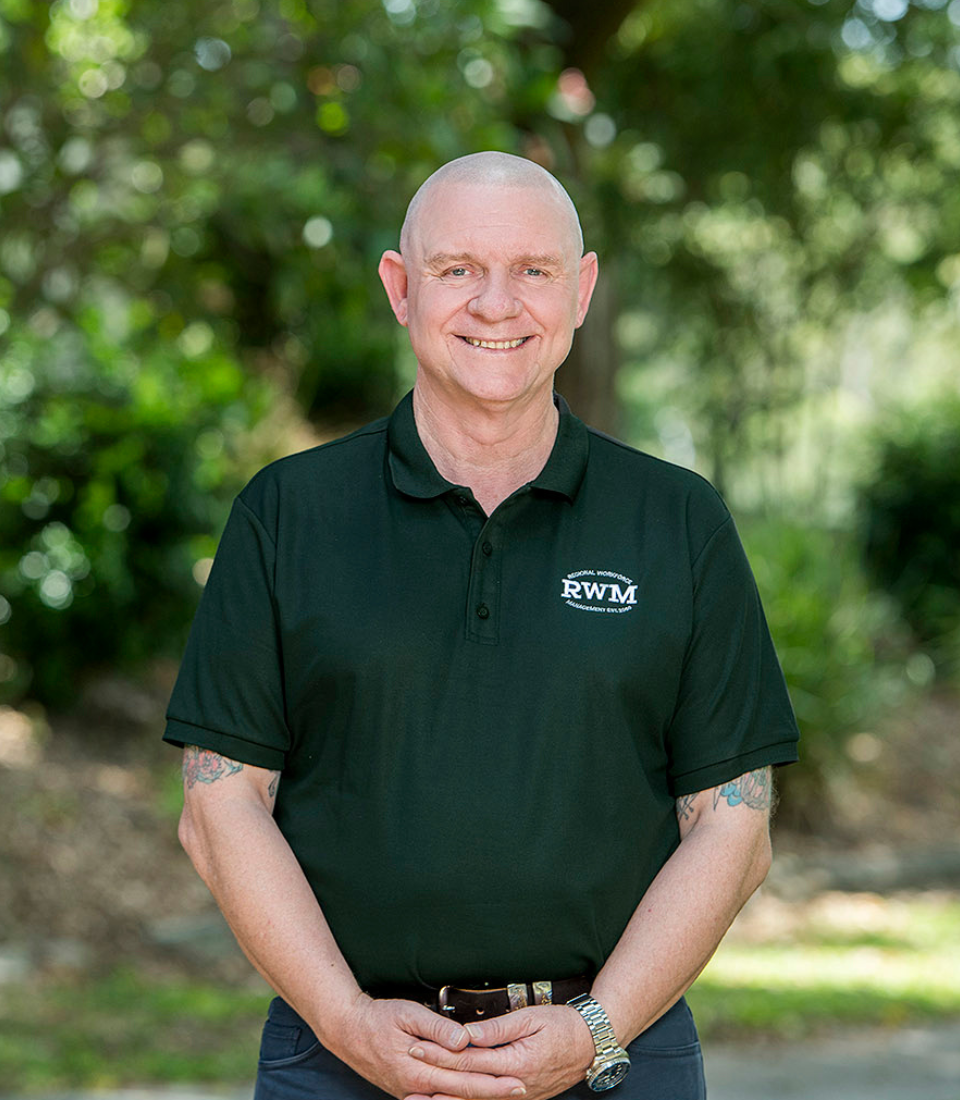 A woman in a denim jacket is smiling with her hand on her chin.