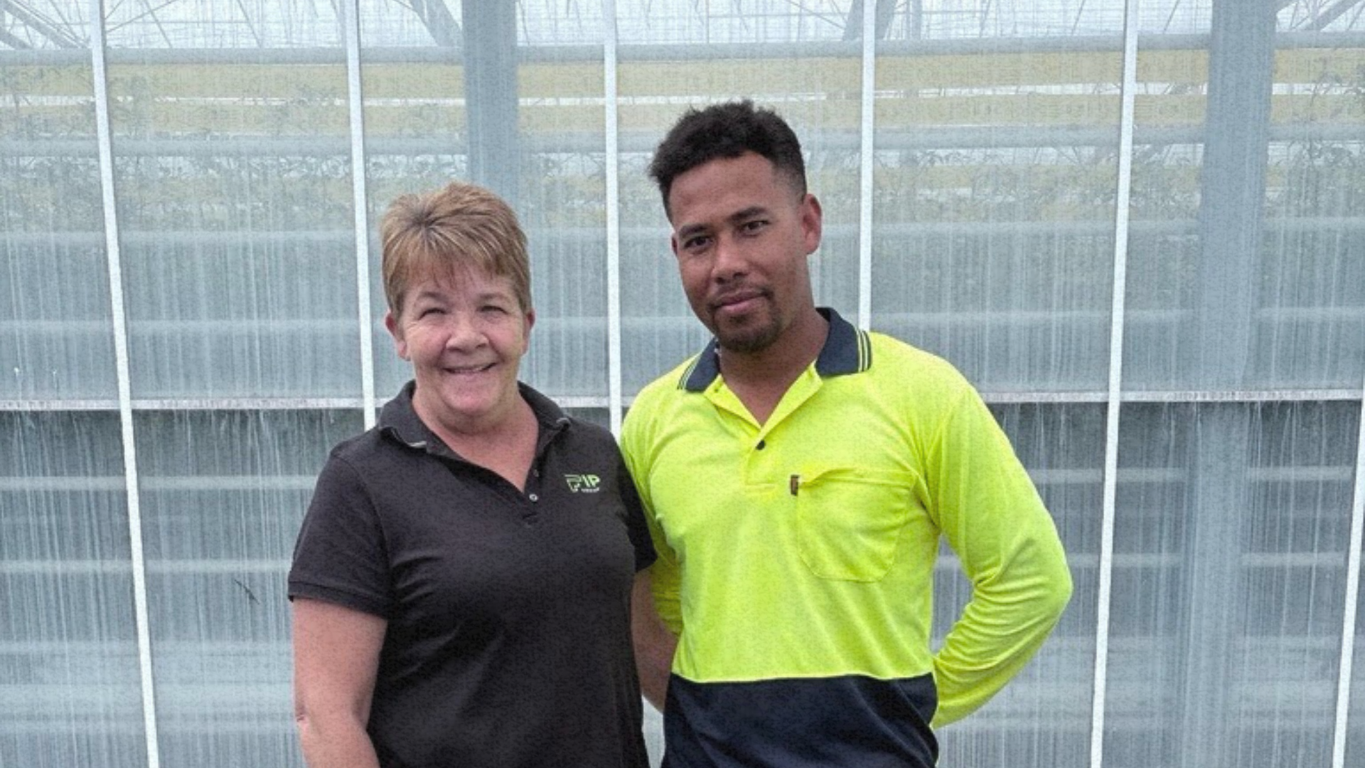 PALM worker Pattson standing with a woman in front of a newly built green house, representing his achievements through the program.