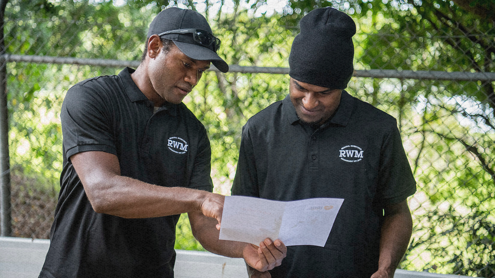 Two workers in black RWM shirts reviewing information on certificates, one pointing while the other 