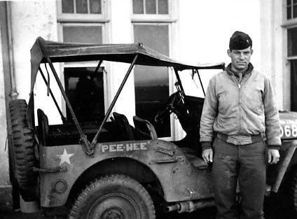 A man is standing next to a jeep that says pce-hee on it.