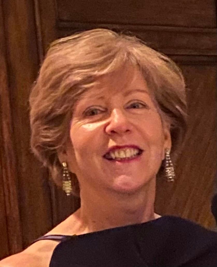 A smiling woman with shoulder-length hair and long, dangling earrings against a dark wooden background.