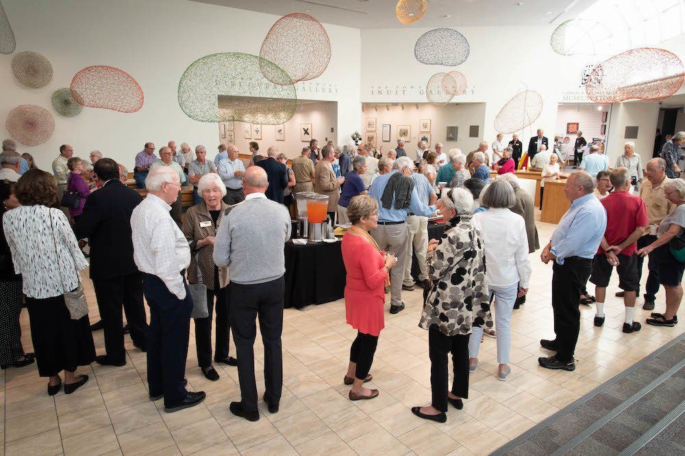 A large group of people are standing in a room talking to each other.