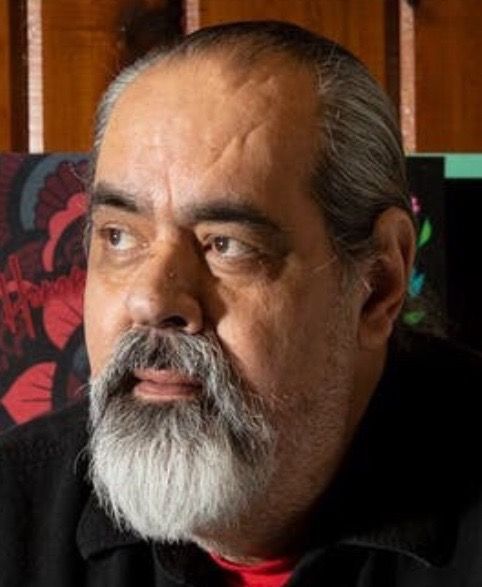 Man with graying beard and hair, looking left, indoors.