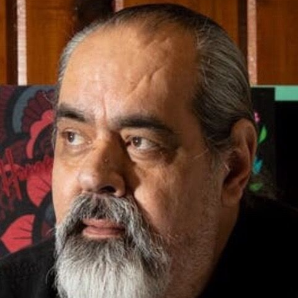 Man with gray beard looking to the side, wearing a dark shirt.