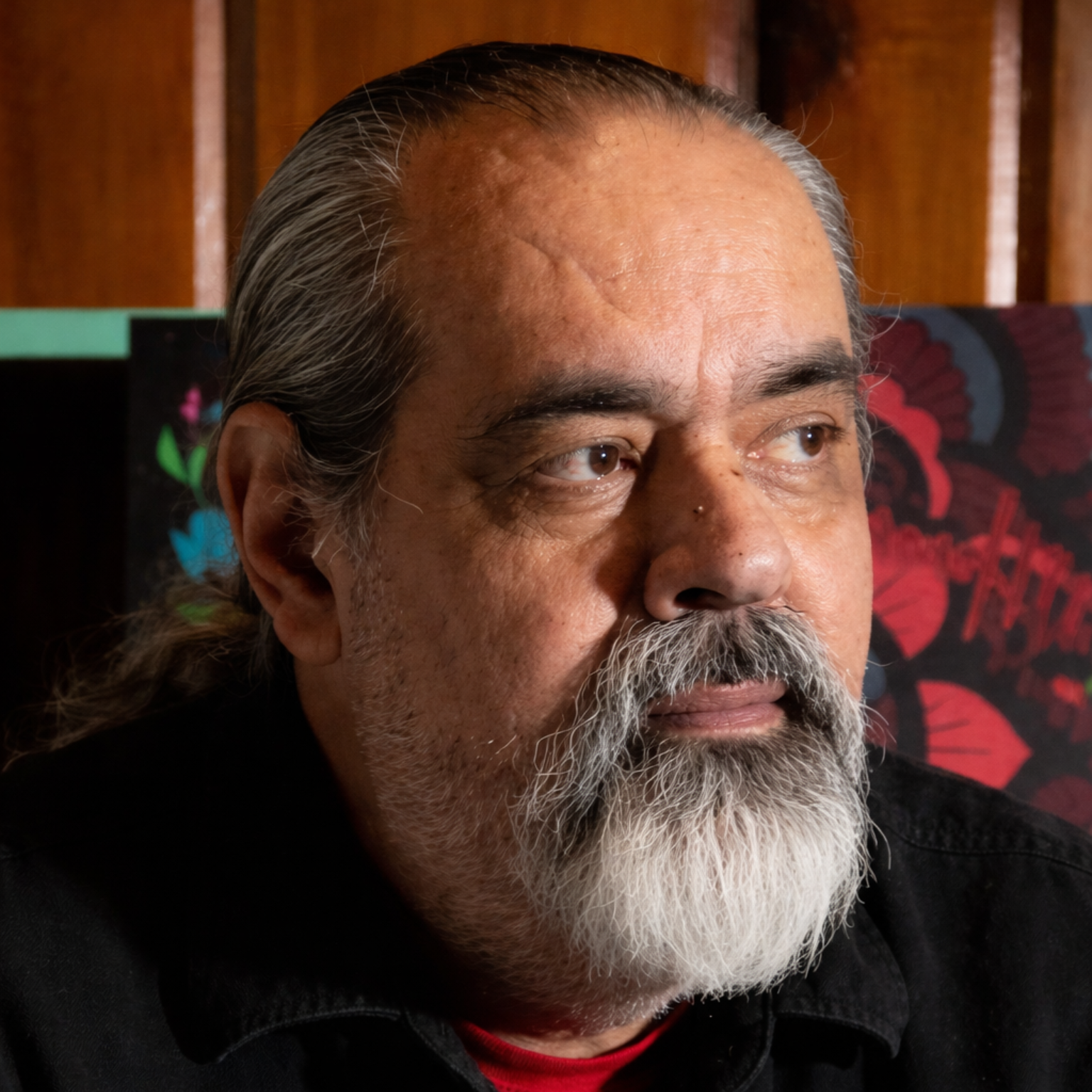Man with graying beard and hair, looking left, indoors.
